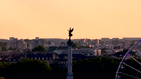 Column-Monument-of-Girondins-with-winged-victory-sculpture-and-Ferris-Wheel-in-Bordeaux-France-during-sunset,-Aerial-hover-shot