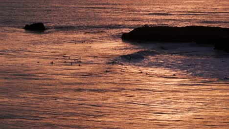 Drone-aerial-view-of-sunset-in-Santa-Cruz,-California-with-surfers-catching-waves