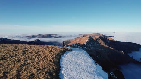 Eine-Person-Steht-Auf-Einem-Bergrücken,-Umgeben-Von-Schnee-Und-Wolken-Darunter,-Im-Nationalpark-Vulkane-Des-Zentralmassivs-Der-Auvergne-In-Frankreich