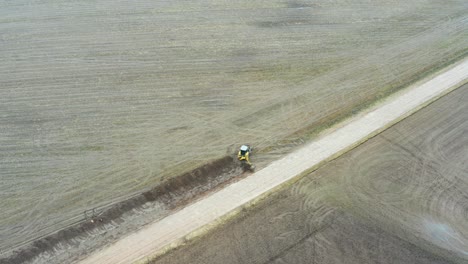 Luftaufnahme-Eines-Traktorbaggers-Auf-Einem-Feld,-Der-Einen-Entwässerungsgraben-In-Der-Nähe-Einer-Schotterstraße-Ausgräbt