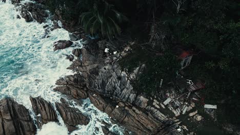 Toma-De-órbita-Aérea-De-Una-Pequeña-Cabaña-En-Un-Acantilado-Rocoso-De-La-Costa-Con-Espumosas-Olas-Blancas-Chapoteando-En-Tierra