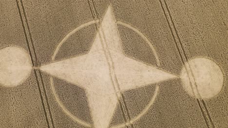 Curious-geometric-crop-circle-in-dry-brown-farm-land,-twisting-aerial-riser