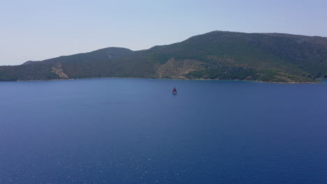 Panoramic-drone-shot-of-a-sailboat-with-red-sails-that-is-sailing-offshore-on-a-clear-summer-day