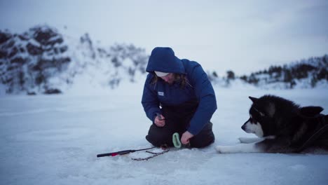 Un-Hombre-Con-Su-Perro-A-Su-Lado-Está-Limpiando-El-Pescado-Que-Pescó-Mientras-Pescaba-En-El-Hielo-En-Bessaker,-Condado-De-Trondelag,-Noruega---Toma-Estática