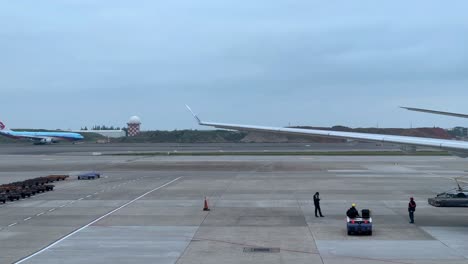 Ground-crew-signaling-to-a-large-airplane-at-an-airport-tarmac,-overcast-sky,-potential-for-rain