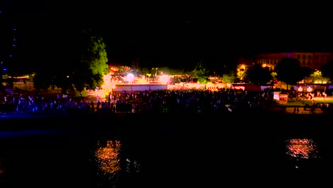 Garonne-river-shore-with-Wine-fair-illuminated-with-large-crowds-at-night-in-Bordeaux-France,-Aerial-tilt-down-approach-shot