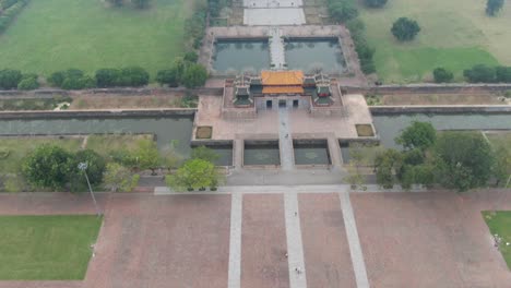 Drone-aerial-view-in-Vietnam-flying-over-Hue-imperial-stone-brick-fortress-wall,-green-gardens,-temples-and-small-buildings-on-a-cloudy-and-foggy-day