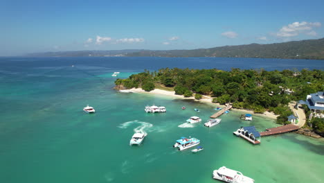 Vuelo-Aéreo-Hacia-Atrás-En-Una-Isla-Inclinando-La-Cámara,-Con-Barcos-Y-árboles,-El-Caribe,-República-Dominicana