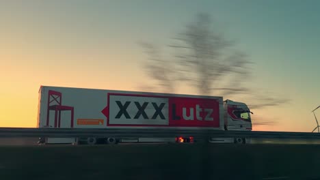 Xxxlutz-Lieferwagen-Fährt-Bei-Sonnenuntergang-Auf-Autobahn-Vor-Windrädern-Vorbei