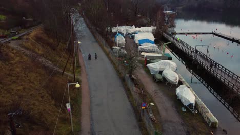 Aerial-tilt-up-of-people-walking-by-shipyard-at-Arstaviken,-Stockholm