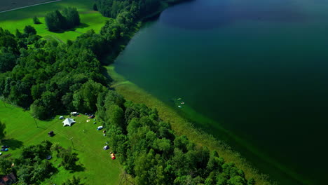 Hermoso-Lago-En-Bosque-Verde,-Gente-Acampando-Y-Barcos-En-La-Orilla-Del-Lago