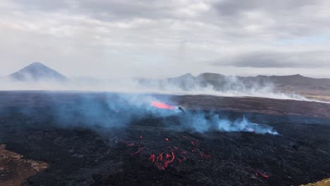 Flujos-De-Lava-En-Fagradalsfjall,-Escena-Llena-De-Humo-Con-Montañas-Como-Telón-De-Fondo,-Luz-Del-Día