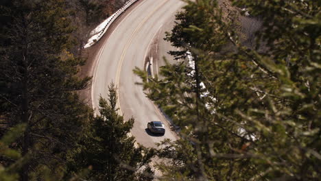 Cars-drive-along-a-winding-mountain-road-in-the-forest,-long-lens