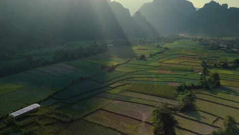 Beautiful-sun-rays-shining-over-mountainous-background-with-mystic-fertile-valley-and-patchwork-crops-in-limestone-valley,-Vang-Vien,-Laos