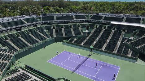 Tennis-Stadium-in-Crandon-Park,-Key-Biscayne,-Miami-USA,-Aerial-View-of-Empty-Stands-and-People-Playing-Doubles,-Dynamic-Drone-Shot