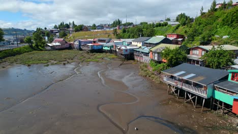 Colorful-stilt-houses-on-chiloe-island-with-low-tide-exposing-the-seabed,-sunny-day,-aerial-view