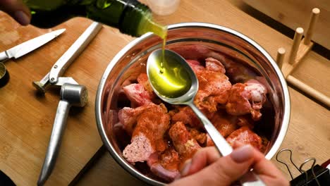 Top-view-of-woman-hands-adding-oil-on-raw-chicken-pieces-with-spices-in-a-metal-bowl-on-wooden-countertop-in-the-kitchen