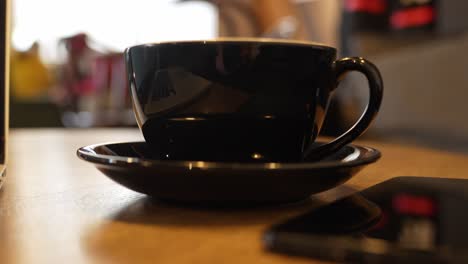 Black-coffee-mug-on-an-office-desk,-close-up-handheld-shot