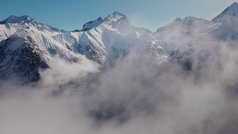 Video-Einer-Drohne,-Die-Durch-Die-Wolken-Auf-Eine-Schneebedeckte-Bergkette-Zufliegt
