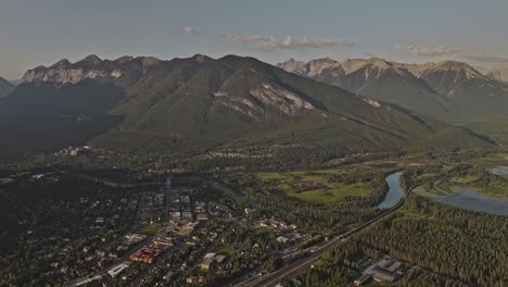 Banff-AB-Canada-Aerial-v31-drone-high-flyover-forested-valley-capturing-views-of-town-center,-railway-train-and-landscape-of-Sulphur-and-Rundle-mountain-ranges---Shot-with-Mavic-3-Pro-Cine---July-2023