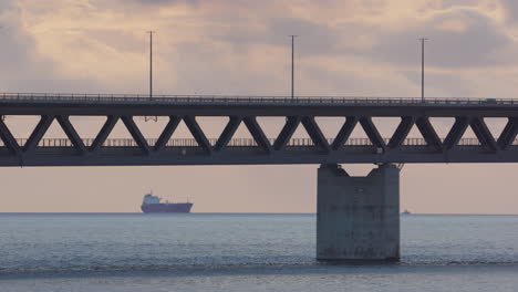 Öresundbrücke-Mit-Verkehr-Vor-Sonnenuntergangshimmel-Mit-Containerschiff-Am-Horizont