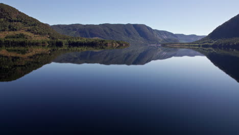 Aerial-pan-over-Byglandsfjord-in-Norway-on-a-sunny-morning,-Forest-covered-mountains-reflect-in-the-rippling-water