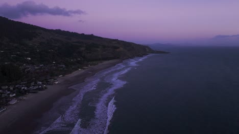 Drone-aerial-view-over-a-beach-with-purple-sky-after-dusk-in-California
