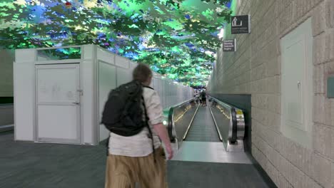 Flight-Paths-art-instillation-in-Hartsfield-Jackson-International-Airport-is-visible-in-the-A-to-B-connecter-tunnel-over-temporary-construction-walls-during-airport-upgrades-with-passengers-passing