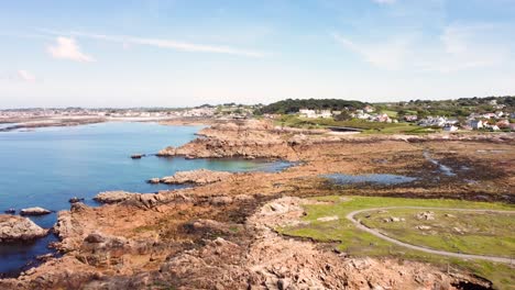 Costa-De-Guernsey-Volando-Sobre-Promontorios,-Bahías,-Rocas-Y-Un-Mar-Azul-Claro-Con-Playas,-Campos-Y-Casas-En-La-Distancia-En-Un-Día-Soleado