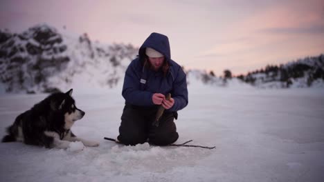 Un-Hombre-Capturó-Con-éxito-Un-Pez-Mientras-Pescaba-En-El-Hielo-Con-Su-Perro-En-Bessaker,-Condado-De-Trondelag,-Noruega---Toma-Estática