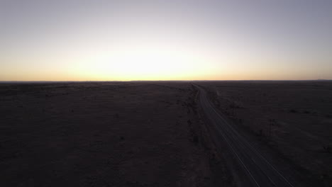 Drone-shot-of-an-empty-remote-desert-highway-at-sunset