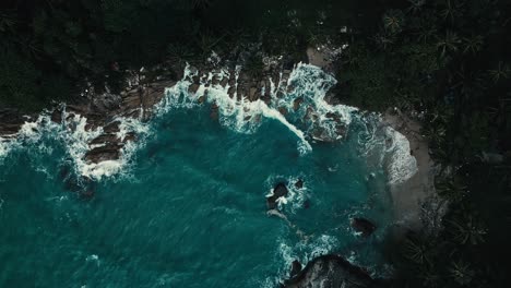 Top-down-view-descending-shot-of-white-foamy-waves-hitting-rocky-coastline-from-blue-oceanic-water