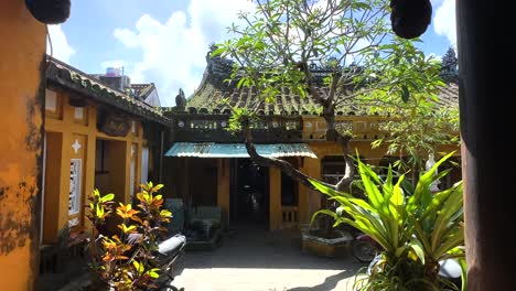 Courtyard-of-Guan-Di-Temple-in-Hoi-An,-Vietnam-with-moss-of-pagoda-roof,-yellow-walls-and-blue-sky