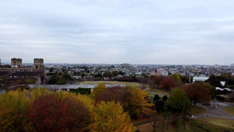 A-park-in-autumn-with-colorful-trees-and-a-distant-castle,-aerial-view