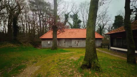 Abandoned-wooden-farm-barn-with-orange-roof-stone-in-forest-in-winter