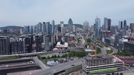 Vista-Aérea-Del-Horizonte-De-La-Ciudad-Moderna-De-Montreal-Quebec-Canadá,-Drones-Vuelan-Sobre-La-Ciudad-Inteligente-Con-Autopista-De-Tráfico-Y-Grúa-De-Construcción