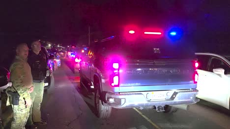 Nighttime-traffic-stop-with-police-presence-and-patrol-car-lights,-civilian-walking-by