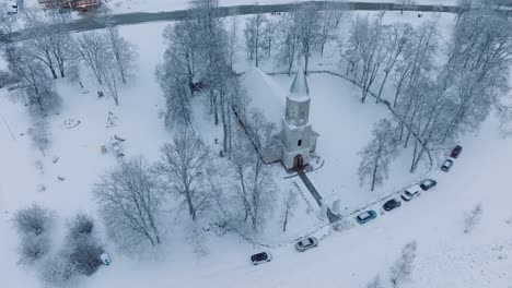 Winter-blankets-a-small-church-and-surrounding-cars-in-a-quaint-Renda-village-,-aerial-birdseye-orbit-view