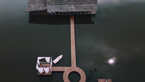 Tilt-up-reveal-shot-drone-footage-of-stilt-house-in-lake-water-with-wooden-rack