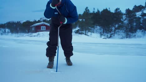 A-Man-is-Manually-Drilling-a-Hole-in-the-Ice-using-an-Ice-Auger-for-Fishing-in-Bessaker,-Trondelag-County,-Norway---Static-Shot