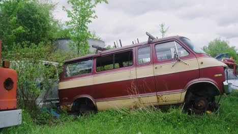 Profile-shot-of-an-old-cargo-van-surrounded-by-other-rusting-vehicles-in-an-abandoned-field