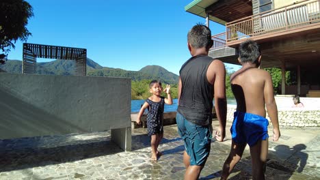 Two-kids-jumping-into-the-pool-of-vacation-house-with-mountainous-background,-dynamic