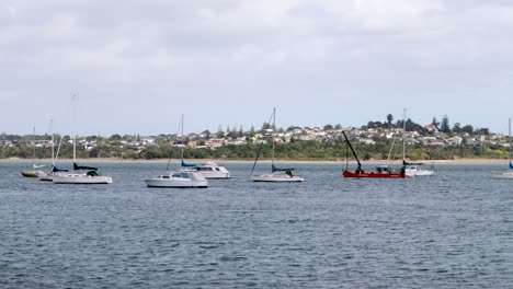A-handheld-shot-of-some-boats-floating-on-a-lake-with-a-neighborhood-in-the-background-in-Auckland,-New-Zealand,-on-a-windy-and-cloudy-day