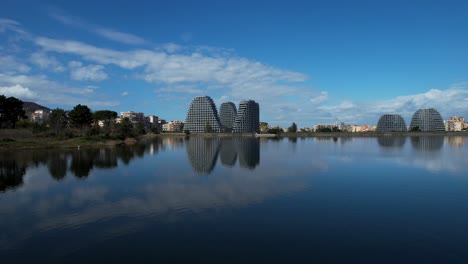 Reflejando-La-Arquitectura-De-Tirana:-El-Horizonte-Urbano-Y-El-Cielo-Azul-Reflejados-En-Las-Tranquilas-Aguas-Del-Lago-Artificial,-Abrazando-El-Diseño-De-La-Ciudad.