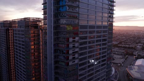 Descending-close-up-aerial-shot-of-the-Oceanwide-Plaza-graffiti-skyscrapers-at-sunset-in-downtown-Los-Angeles,-California