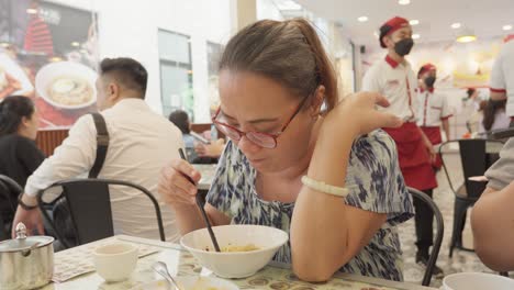 Woman-enjoying-a-bowl-of-noodles-in-a-busy-Indonesian-restaurant,-daylight