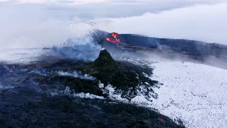 Un-Dron-De-4k-Capturó-Una-Vista-Aérea-Espectacular-Y-única-De-Un-Paisaje-Con-Nieve-Blanca,-Formaciones-De-Lava-Negra,-Niebla-Y-Glaciares,-Con-Lava-Volcánica-En-Erupción-En-El-Centro.