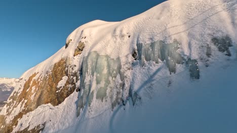 Wall-of-ice-on-a-rock-in-an-evening-sunlight-with-shadows-of-a-ski-tow-in-the-Alps