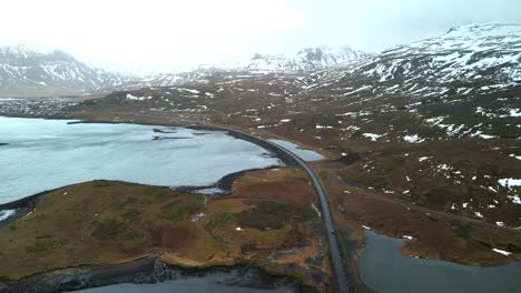 Una-Toma-única-De-Un-Dron-En-4k-Que-Captura-Vistas-Cinematográficas-De-La-Carretera-De-Circunvalación-Y-Muestra-Un-Vehículo-Que-Viaja-Junto-A-Un-Impresionante-Lago-Y-Montañas-Cubiertas-De-Niebla.