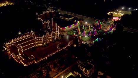 Vista-Aérea-De-Drones-La-Cámara-De-Drones-Avanza-Donde-Muchas-Personas-Están-Estacionando-Afuera-Del-Vehículo-Para-Ver-La-Muy-Buena-Iluminación-Del-Espléndido-Templo-En-El-Interior.